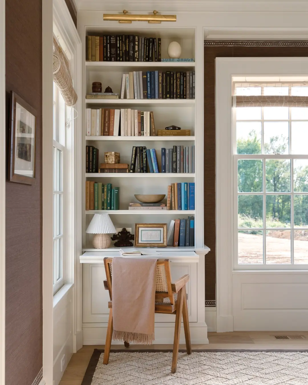 Traditional reading and writing nook with a white built-in bookcase, a recessed secretary desk area, and a light wood and cane chair.