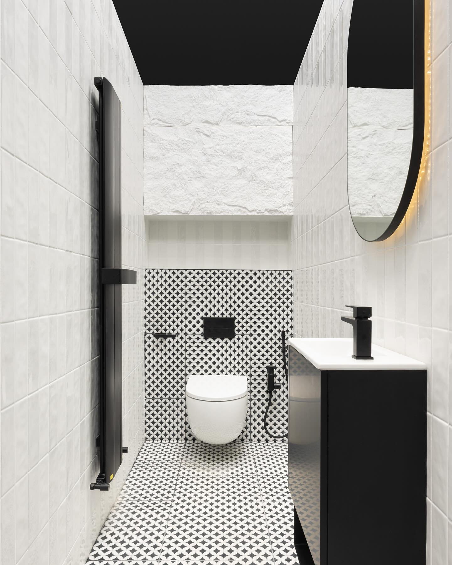 A narrow, monochromatic powder room with black fixtures, white vertical subway tiles, and a floor of small, bold black and white patterned encaustic cement tiles.
