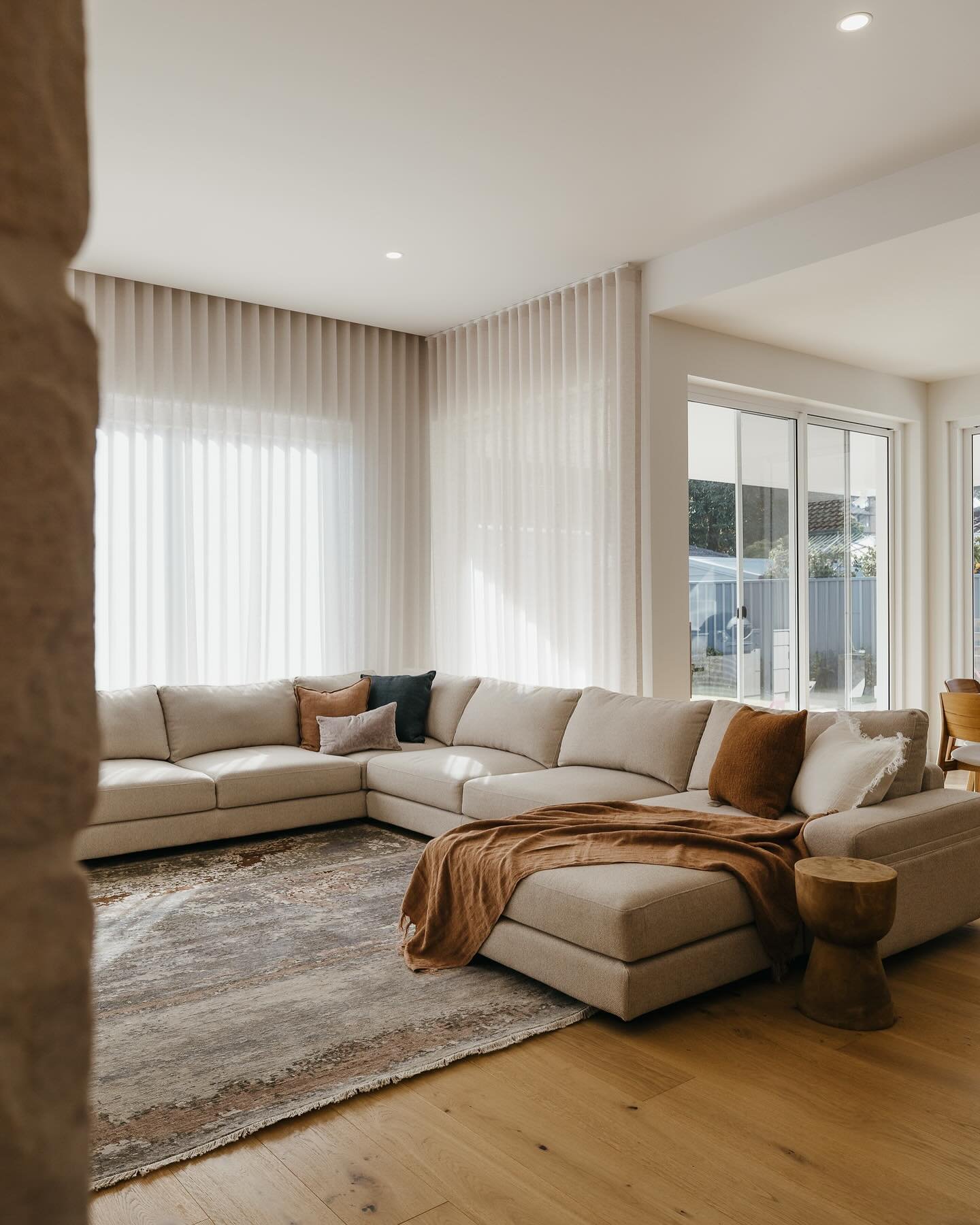 Large, cream L-shaped sectional sofa with a brown throw, sheer curtains, and light wood flooring.