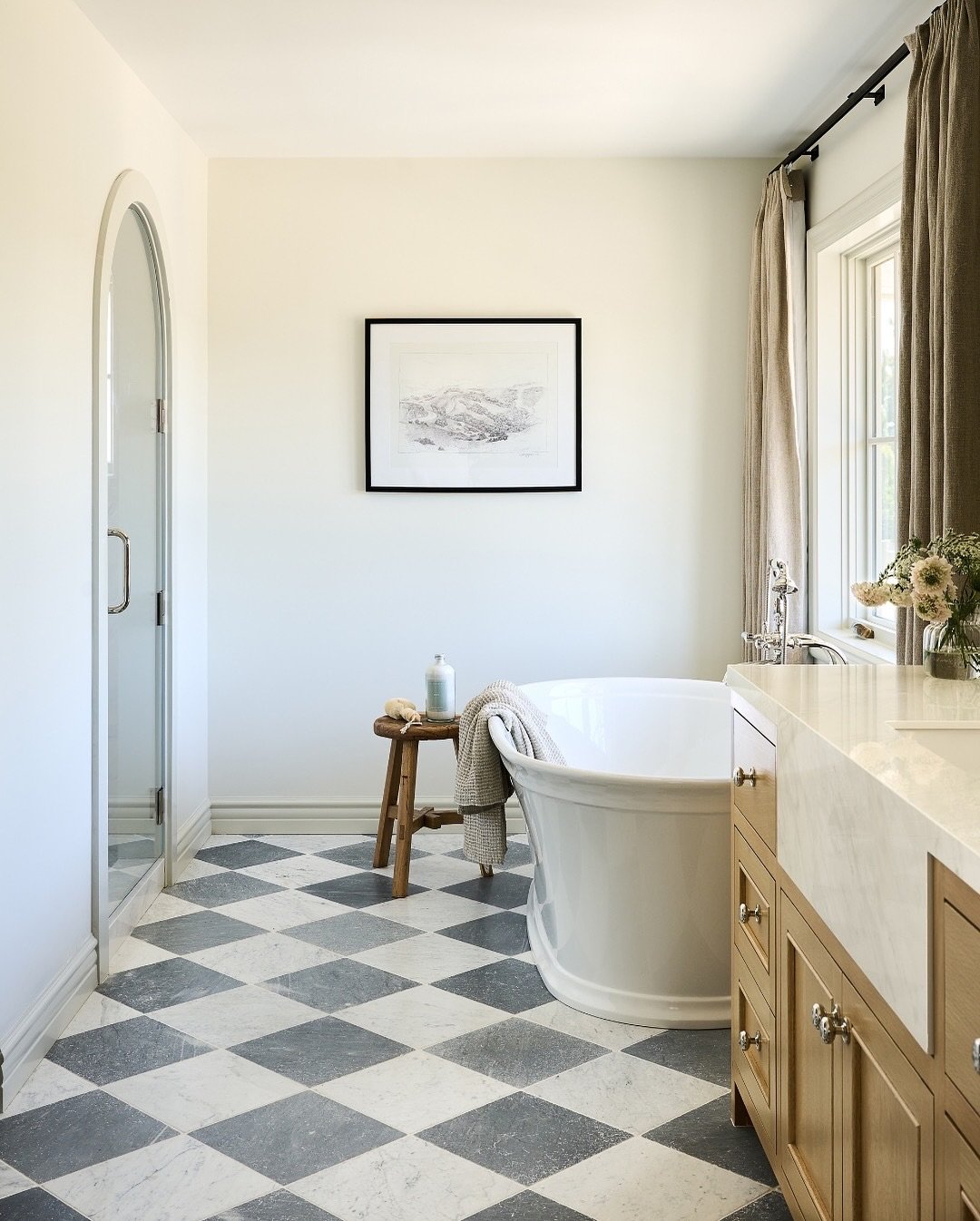 A bright room featuring a floor with large diagonal checkerboard tiles in black gray and white stone next to a freestanding white bathtub.