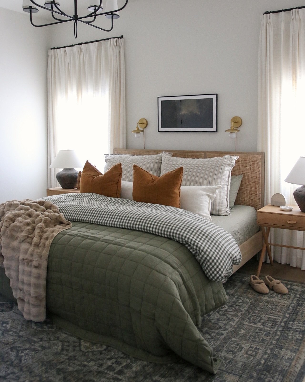 A bedroom featuring a low wicker headboard, an olive green quilted duvet, terracotta accent pillows, and a patterned area rug.