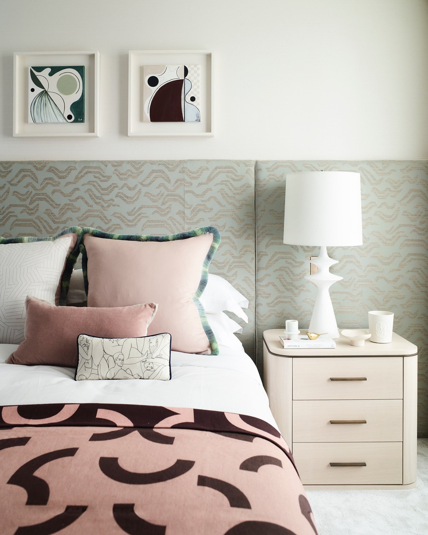Wide, low upholstered headboard in a light sage green fabric with a faint wave pattern, extending across the entire wall width, above a bed dressed in blush and brown linens.