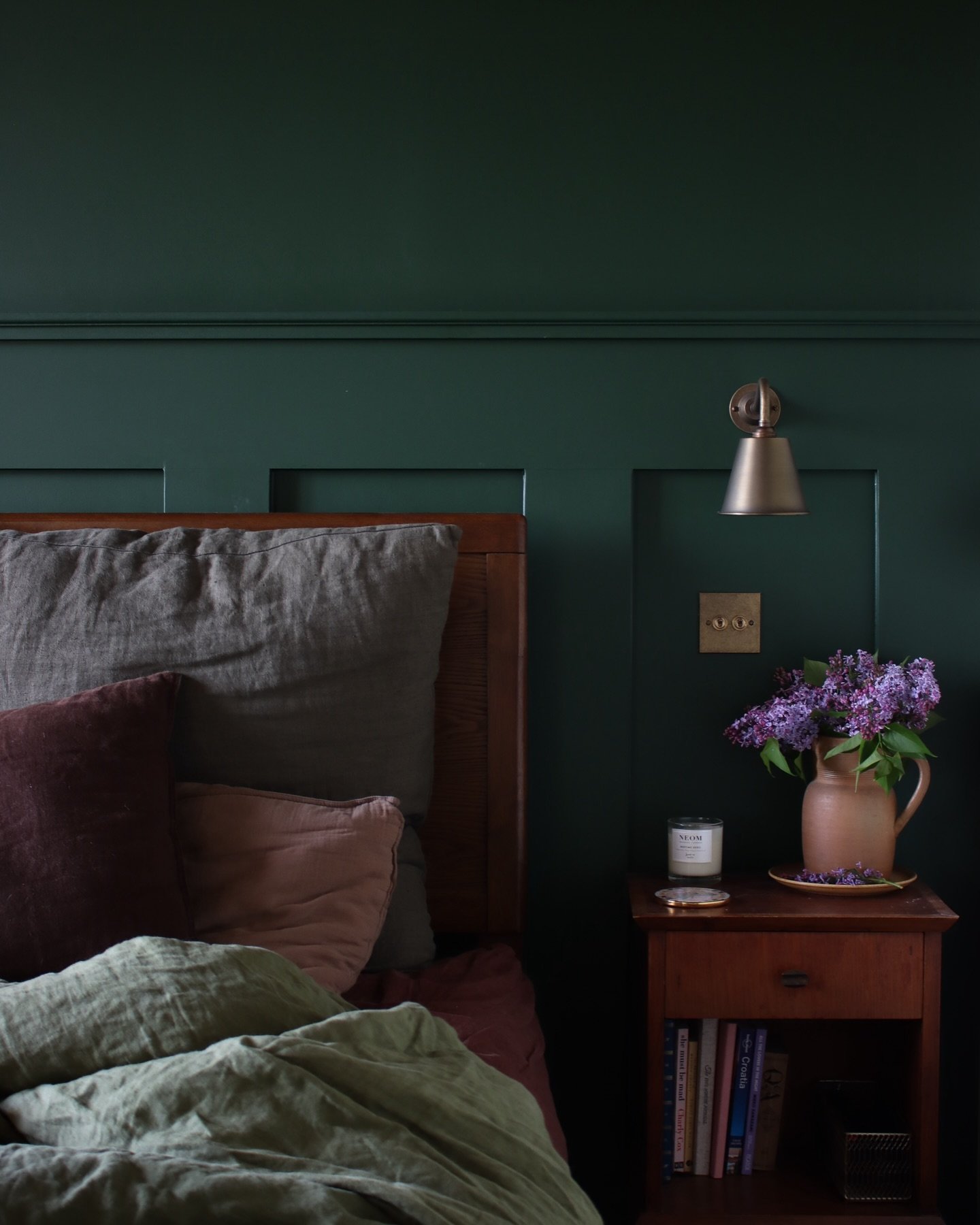 A bedroom with a dark green board and batten accent wall, simple framed art, and a light wood floating nightstand.
