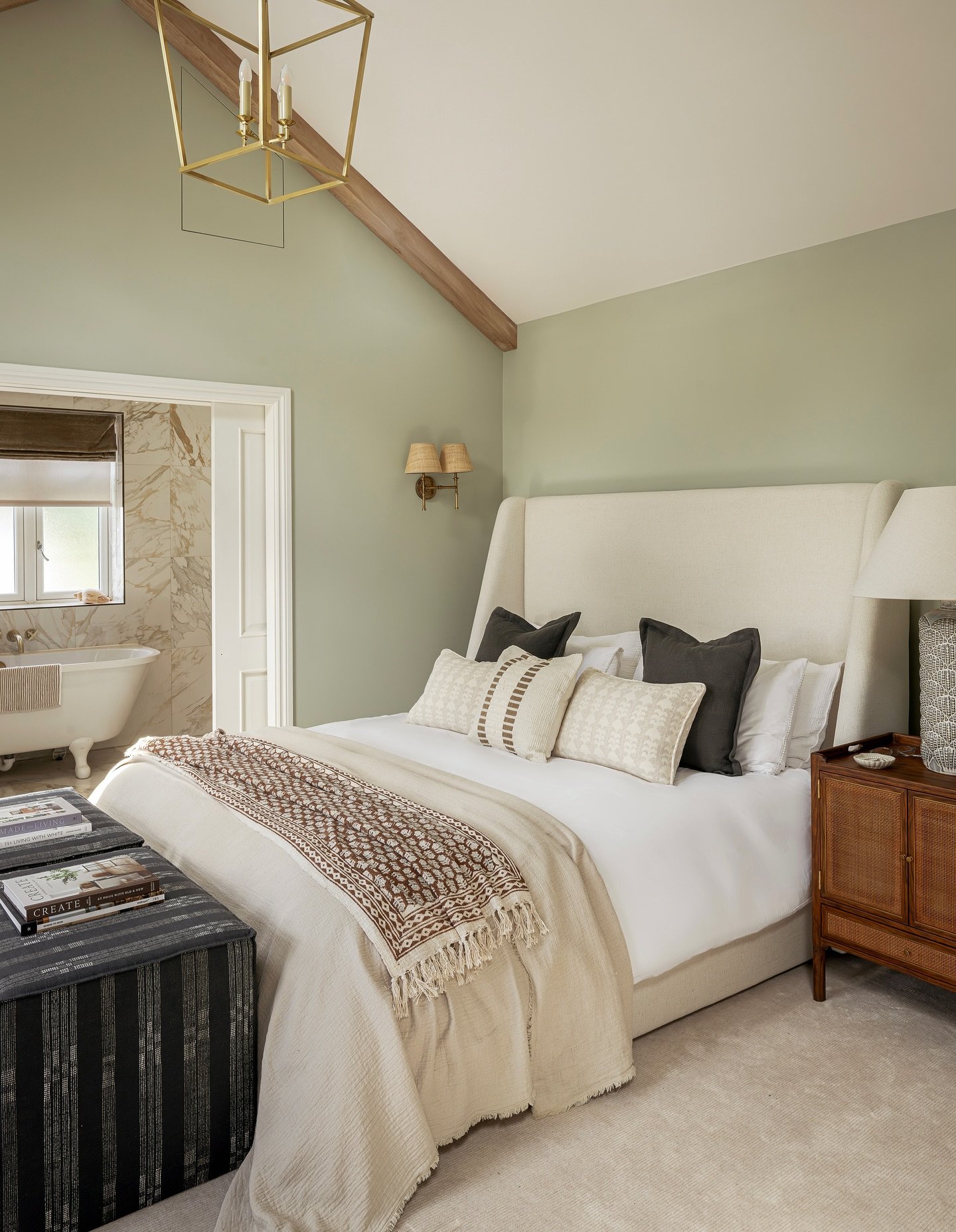High-ceiling farmhouse bedroom painted in soft sage green. Features a tall upholstered bed and natural wood accents.