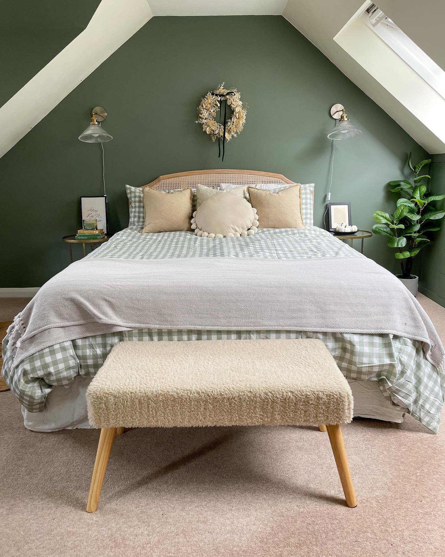Sloping attic bedroom with a sage green accent wall, cane headboard, and gingham bedding.