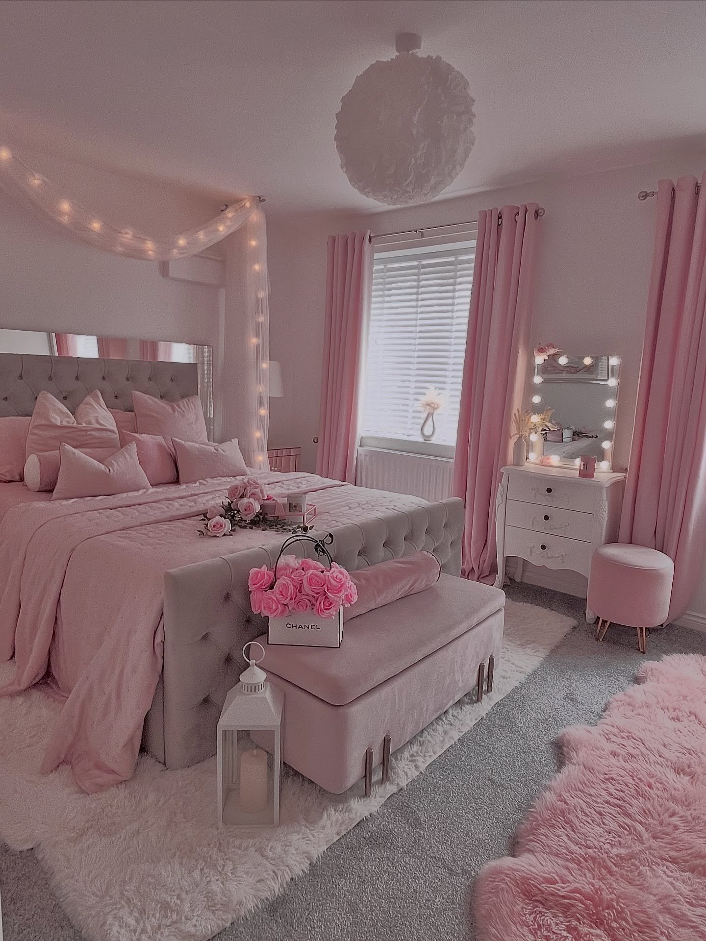 A cozy pink and gray bedroom featuring string lights over the bed, a mirrored vanity, and multiple plush pink rugs.