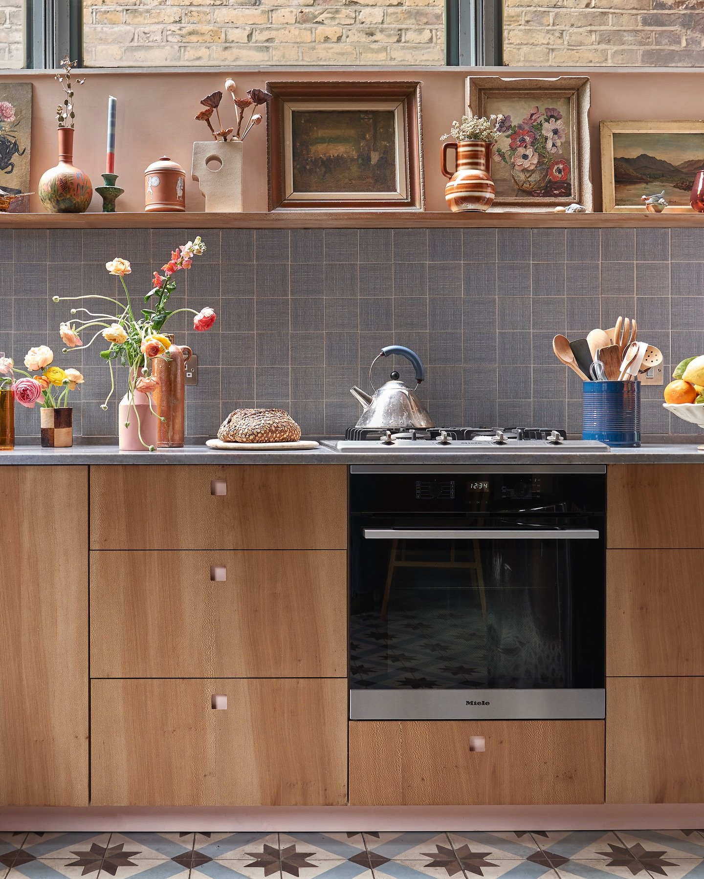 A collection of various framed artworks arranged as a gallery wall next to dark green kitchen cabinetry.