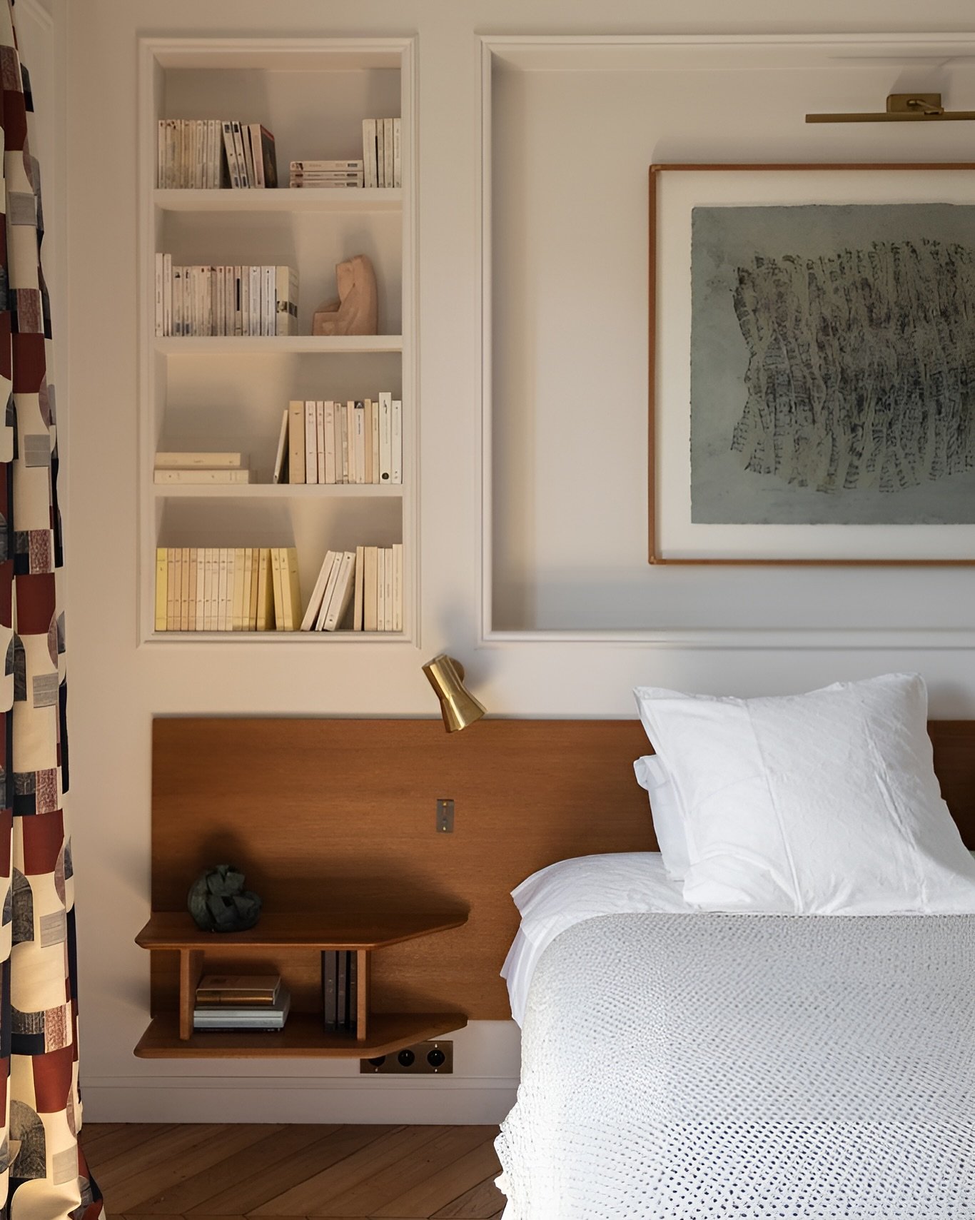 Bedroom featuring a wooden headboard with a floating side shelf and a deep, recessed wall niche filled with books.