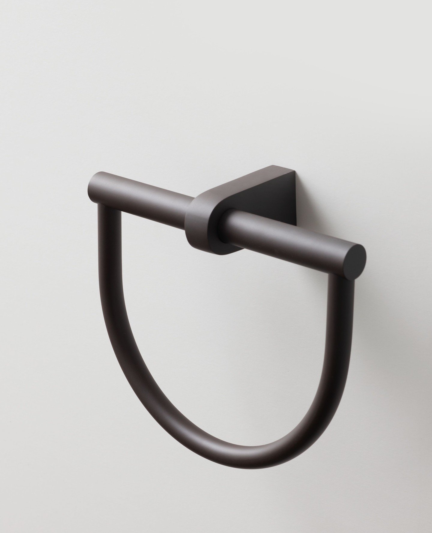 A modern, dark bronze or matte brown open U-shaped towel ring mounted on a light neutral wall.