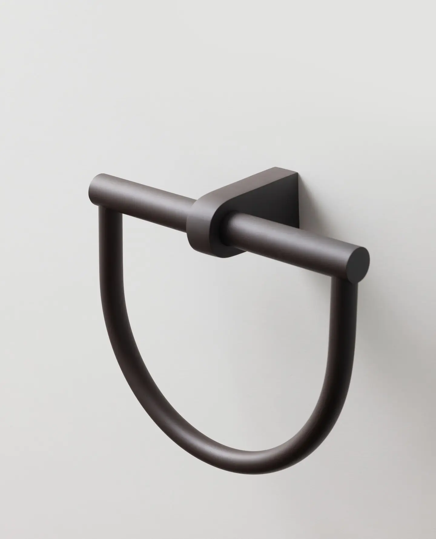 A modern, dark bronze or matte brown open U-shaped towel ring mounted on a light neutral wall.