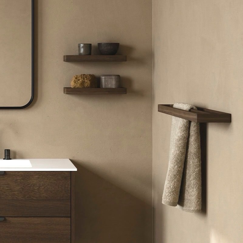 Dark wood towel bar shelf mounted in the corner of a tan wall, with a hand towel draped over the front and resting on top.