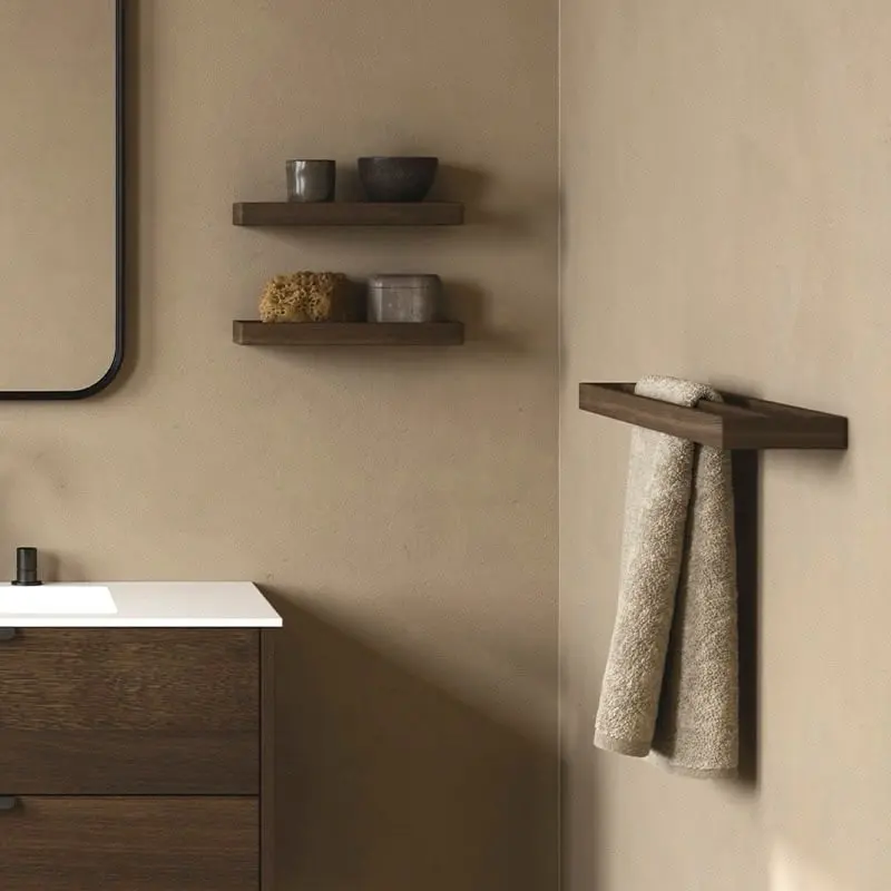 Dark wood towel bar shelf mounted in the corner of a tan wall, with a hand towel draped over the front and resting on top.