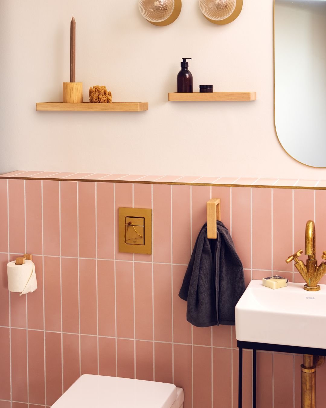 A light natural wood vertical hook holding a dark gray hand towel, mounted on a pink tiled bathroom wall.