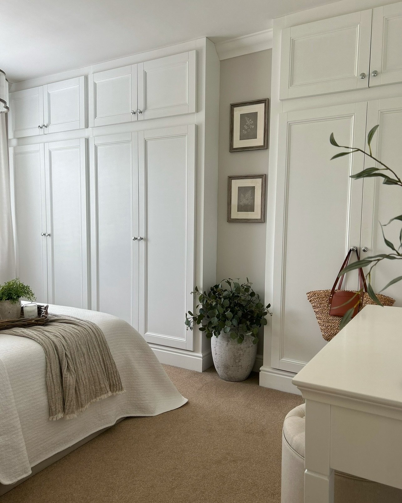 Traditional white floor-to-ceiling built-in wardrobe with shaker-style panels, silver knobs, and upper storage cabinets in a neutral bedroom.