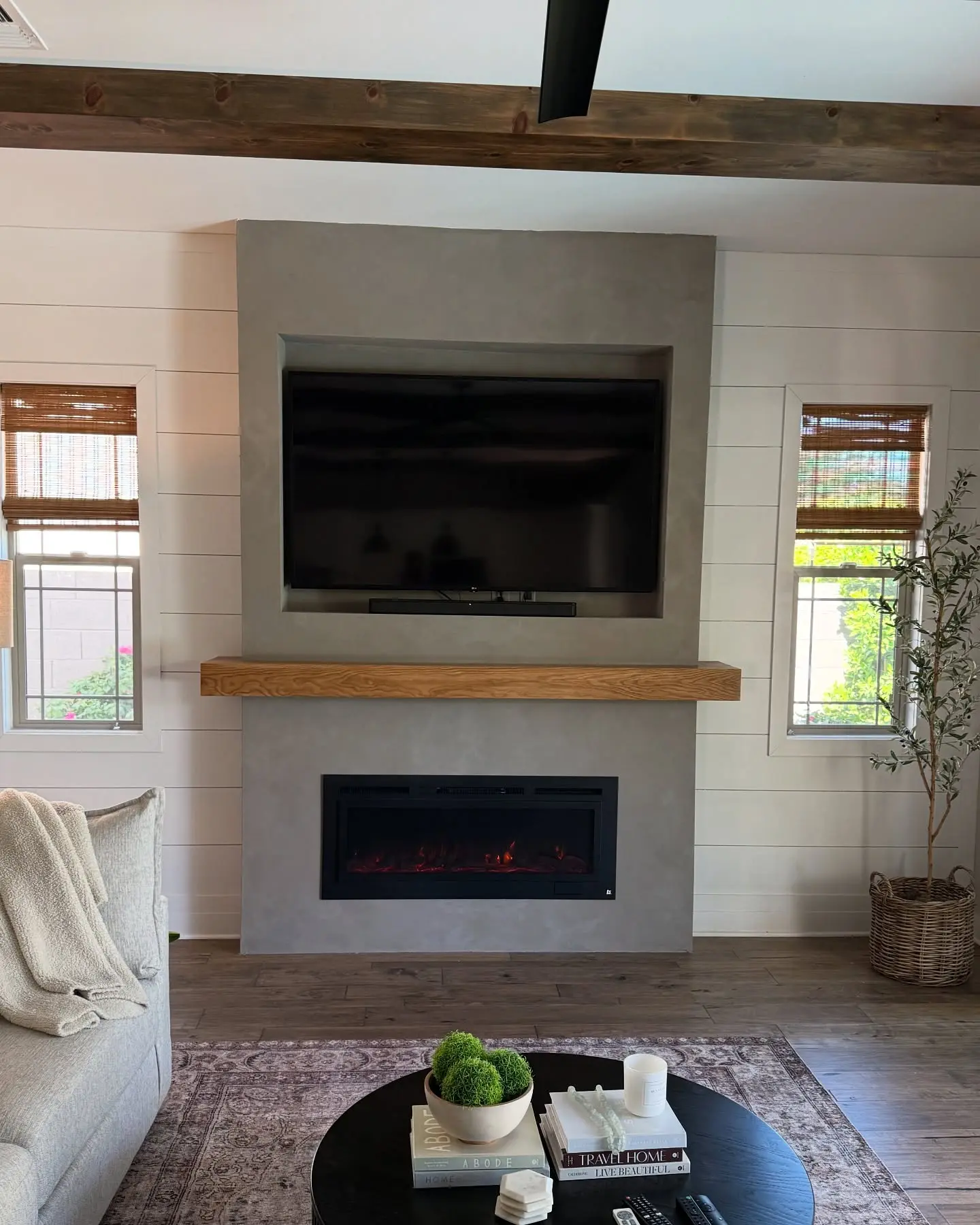 Modern farmhouse living room with a linear electric fireplace set into a floor-to-ceiling grey stucco feature wall below a TV niche and a thick natural wood mantel.