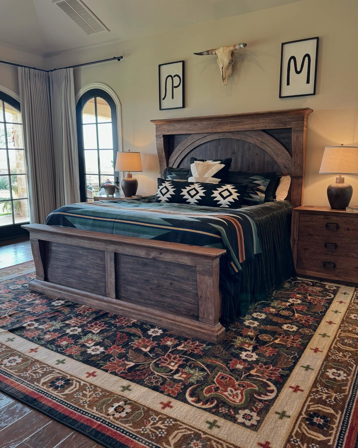 A luxurious Western-style bedroom centered around a massive dark wood sleigh bed with Pendleton-style blankets and ornate arched windows.