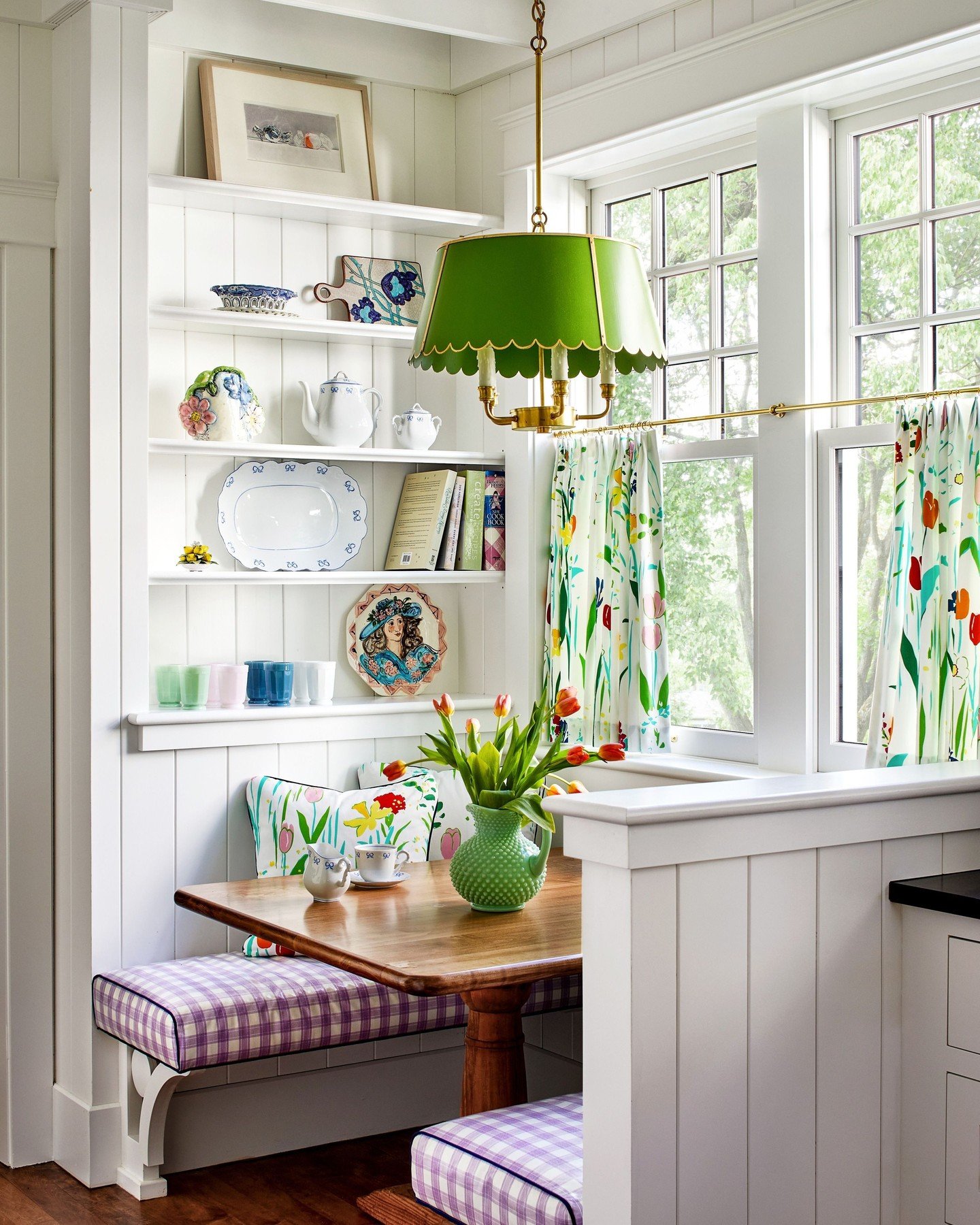 Kitchen breakfast nook with white shiplap paneling and open shelves, featuring white curtains with a vibrant multicolored meadow print on a brass cafe rod.