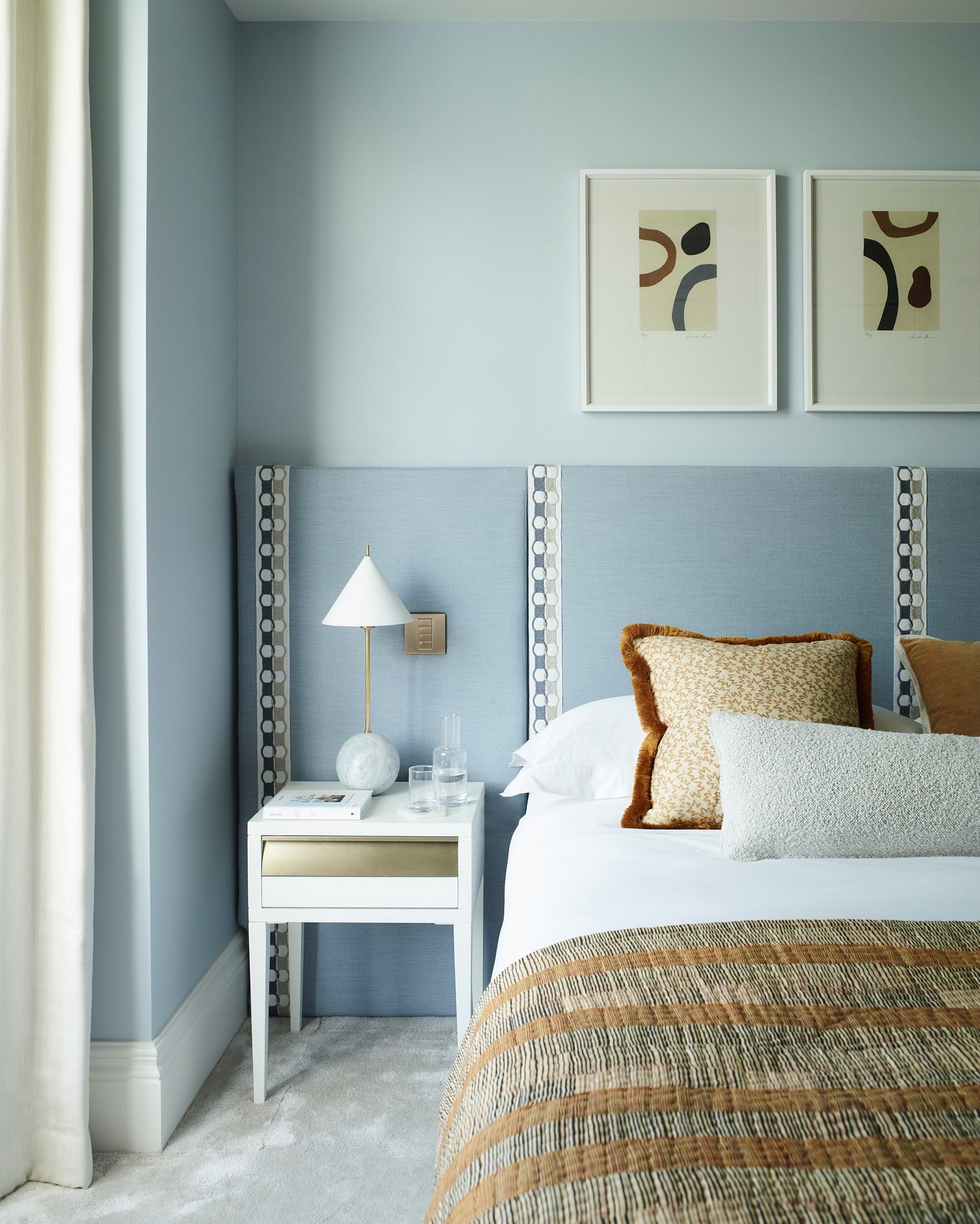 Upholstered headboard in a dusty blue fabric with decorative vertical trim featuring a chain link pattern, against a matching pale blue wall.
