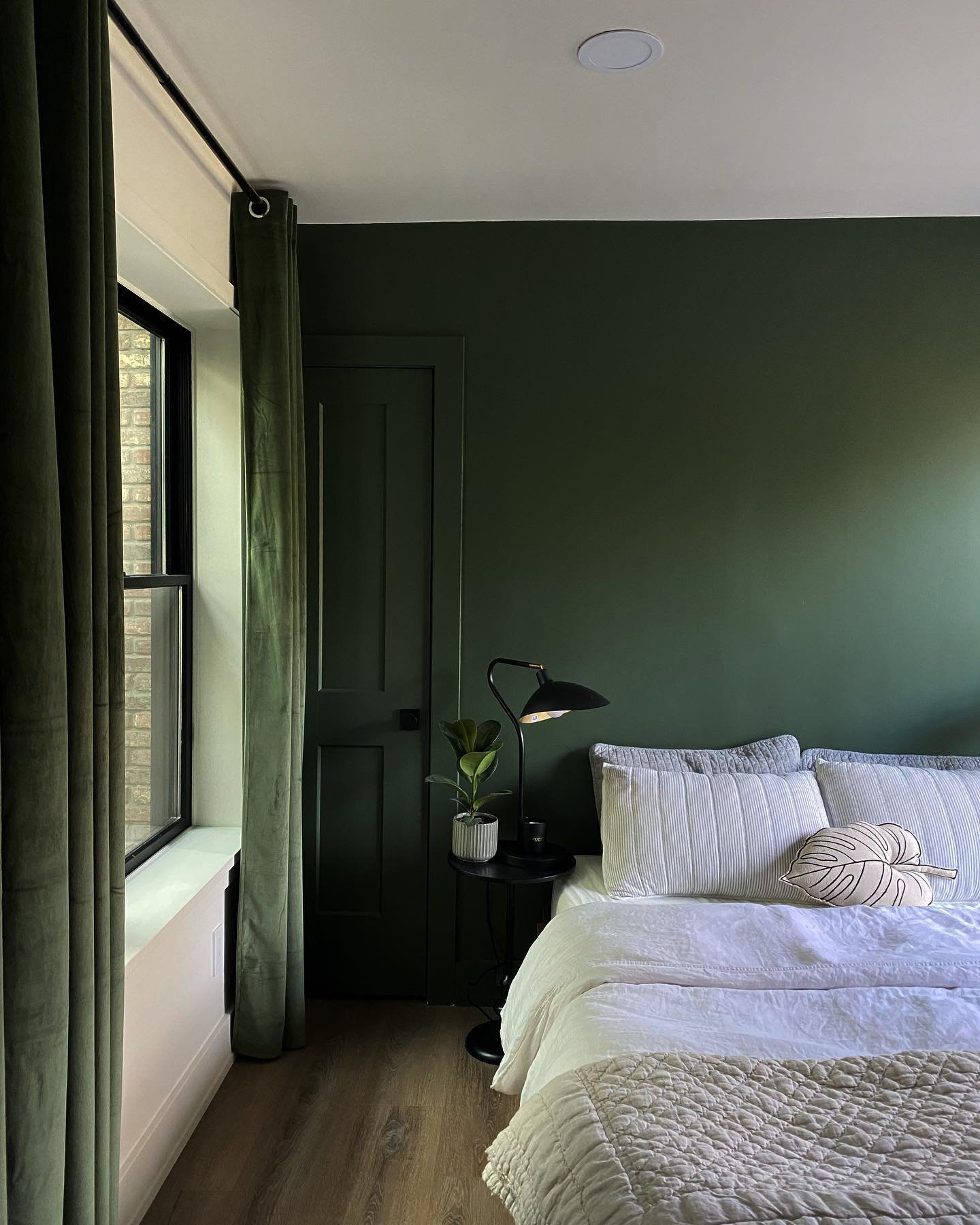A cozy bedroom with a dark green accent wall adorned with a gallery wall of assorted framed art above the bed.