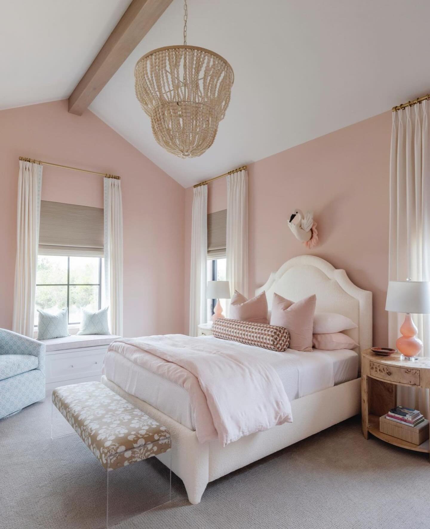Bedroom with soft pink walls, a high vaulted ceiling, a beaded chandelier, and a window seat.