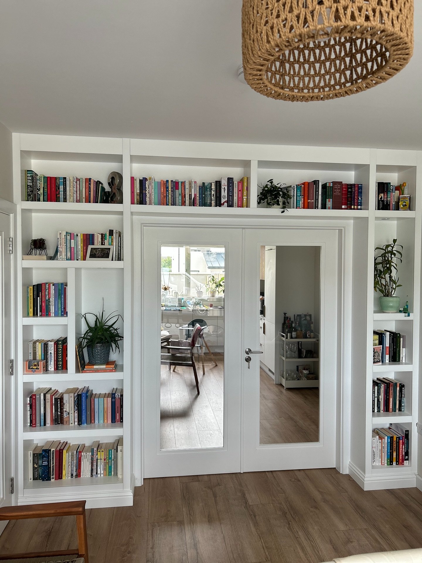 Custom white built-in bookcases flanking and spanning the top of a set of French doors with glass panes, filled with books and small houseplants.