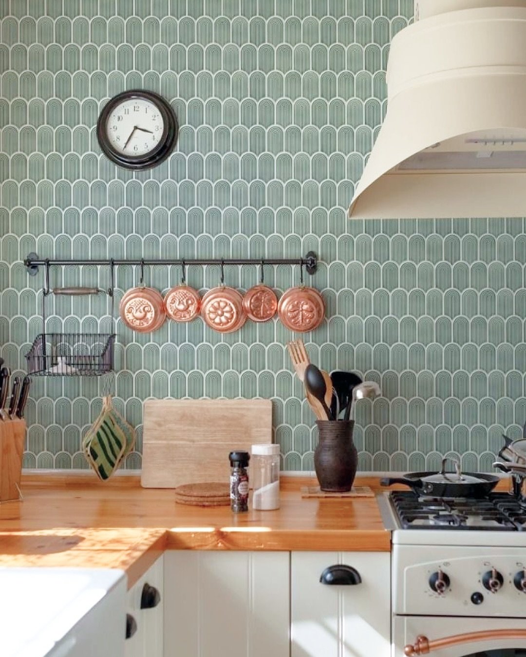 Kitchen with floor-to-ceiling backsplash of sage green and white fan or scallop-patterned tiles, featuring wood countertops and copper pots.