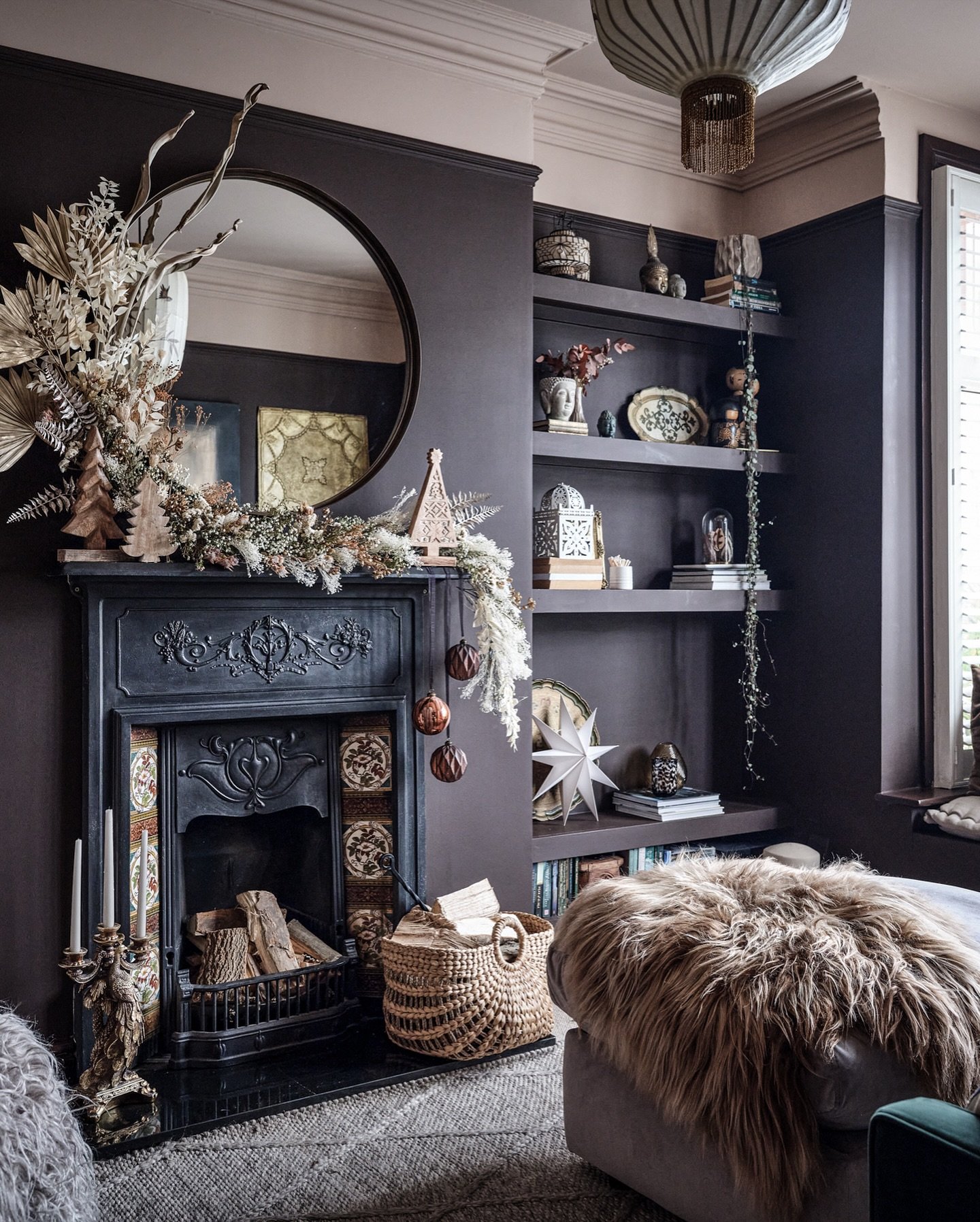 Dark, ornately carved fireplace mantel with a round mirror and a garland made of dried botanicals and wooden decorations.