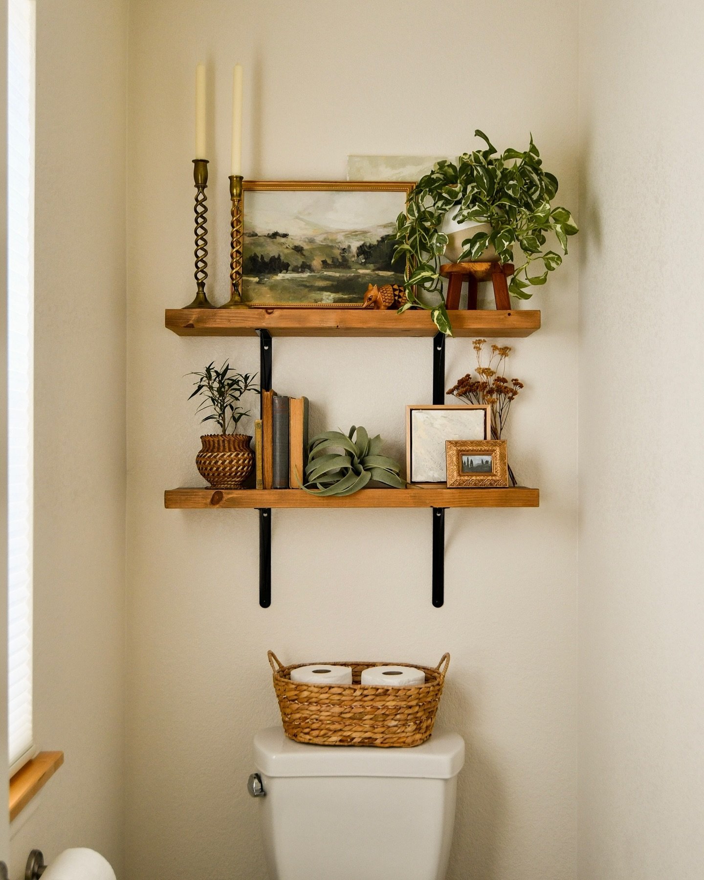 Two rustic wooden shelves with black metal brackets styled with books, plants, framed art, and tall candlesticks.