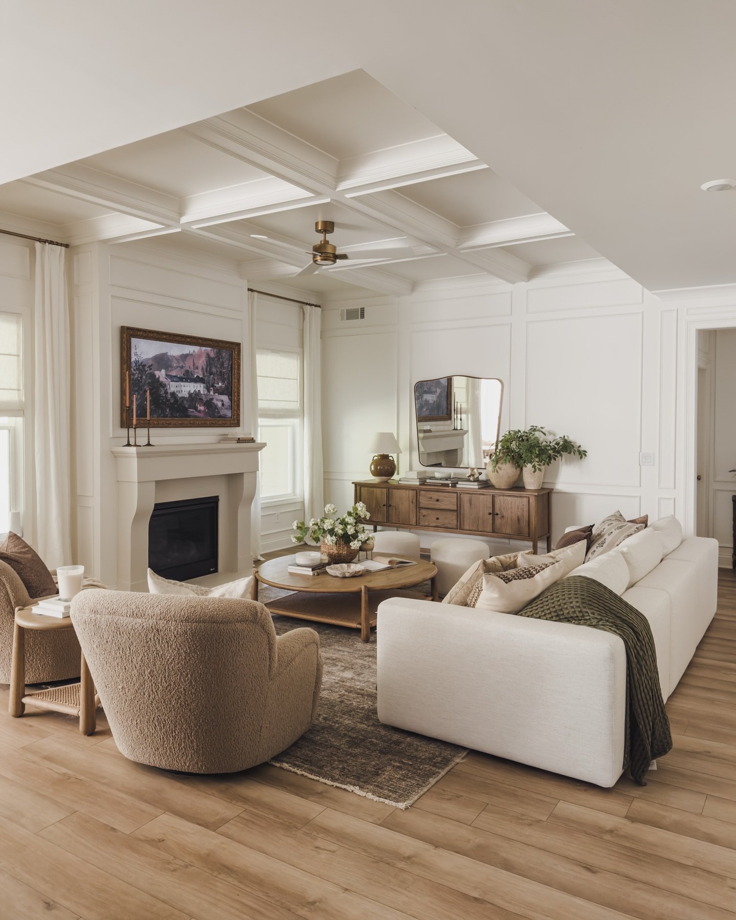 A white living room with elegant wall paneling, a stone fireplace, a bright white sofa, and two plush, beige, rounded teddy-bear fabric armchairs.