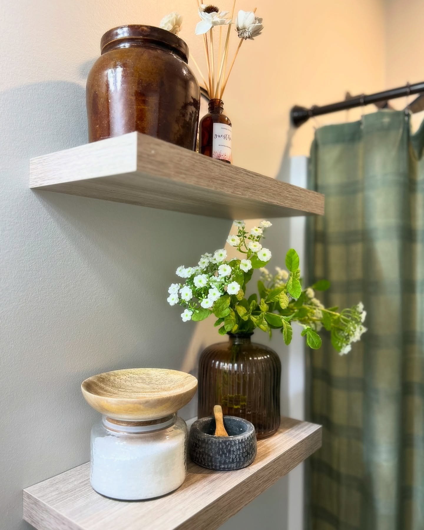 A close-up view of two light oak-colored floating shelves styled with a brown vase, a diffuser, and a small flower arrangement.