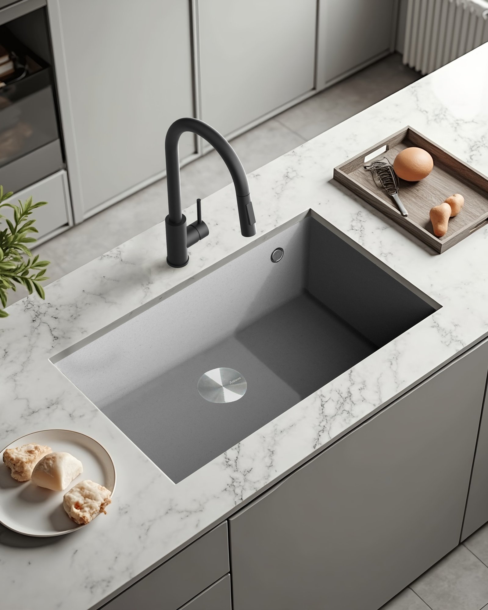 A contemporary, light gray single-bowl sink with a subtle texture, undermounted into a white marble-effect countertop, featuring a matte black faucet.
