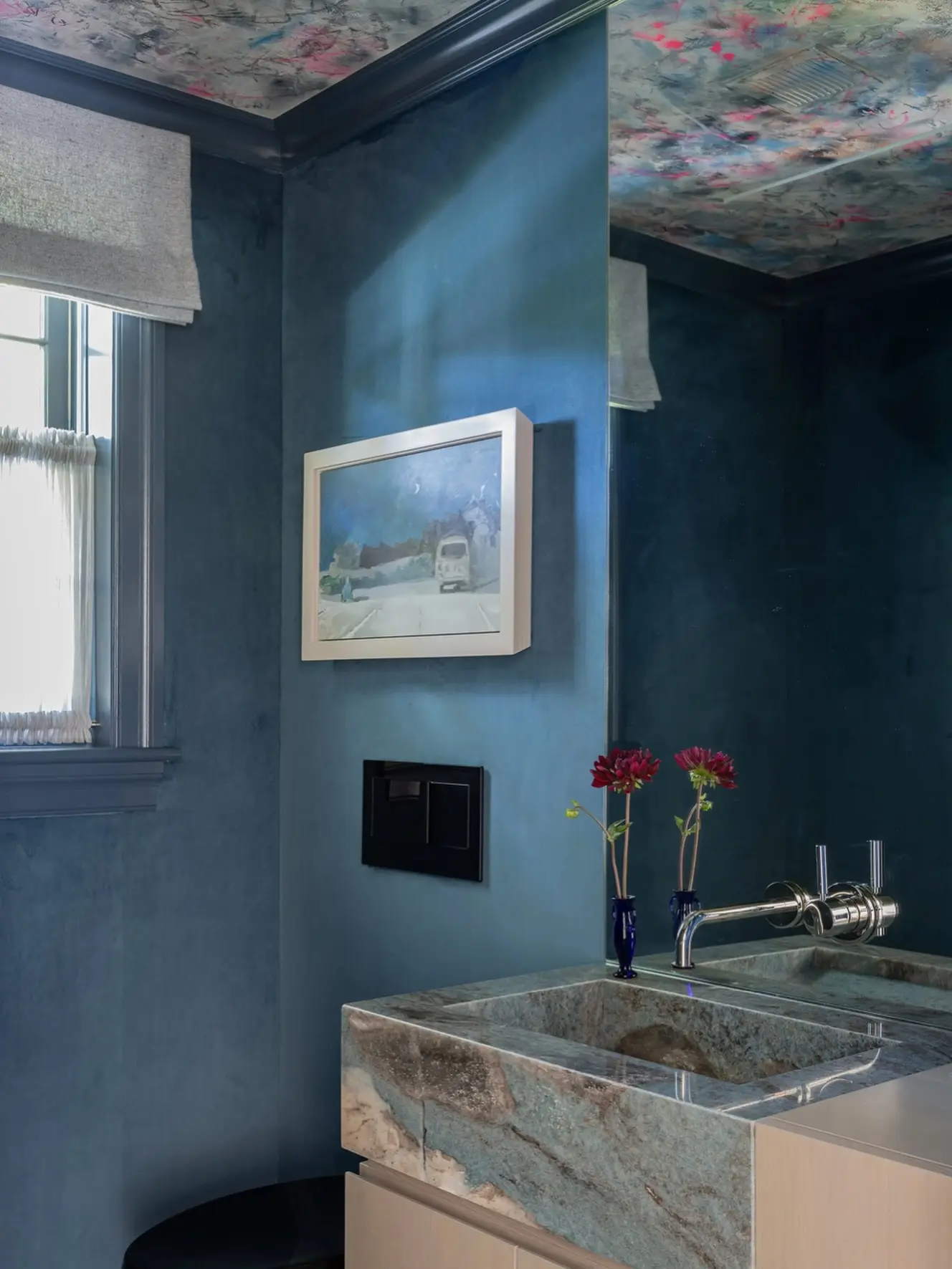 A small oil painting in a white frame mounted on a deep teal-blue Venetian plaster wall above a blue marble sink.