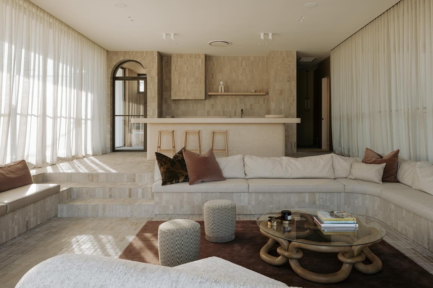 Sunken living room with curved built-in seating, terracotta tile steps, sheer curtains, and a stone-clad bar area.