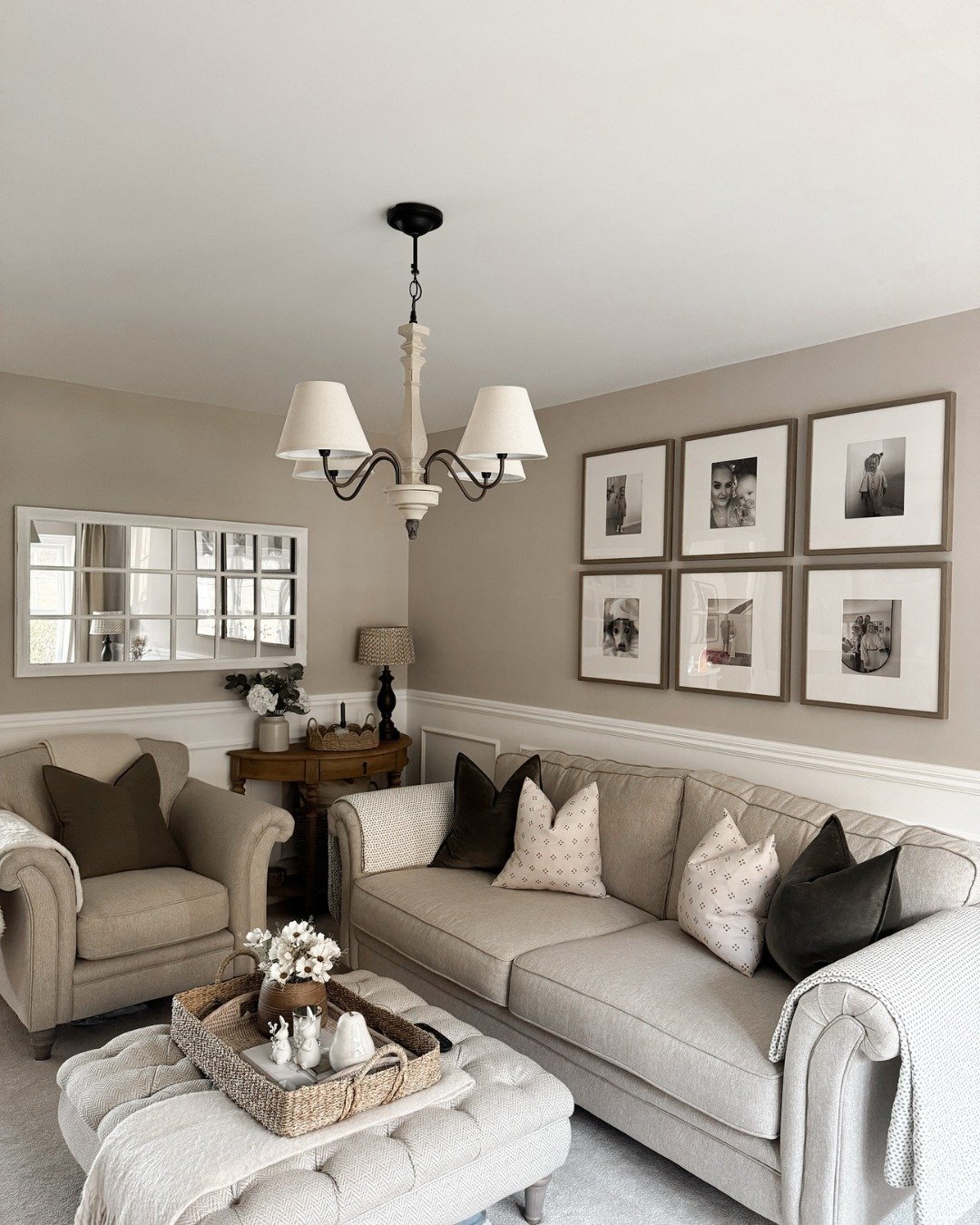 A small, inviting living room with a beige sofa, matching armchair, a tufted ottoman, and a symmetrical gallery wall of framed black-and-white photos.