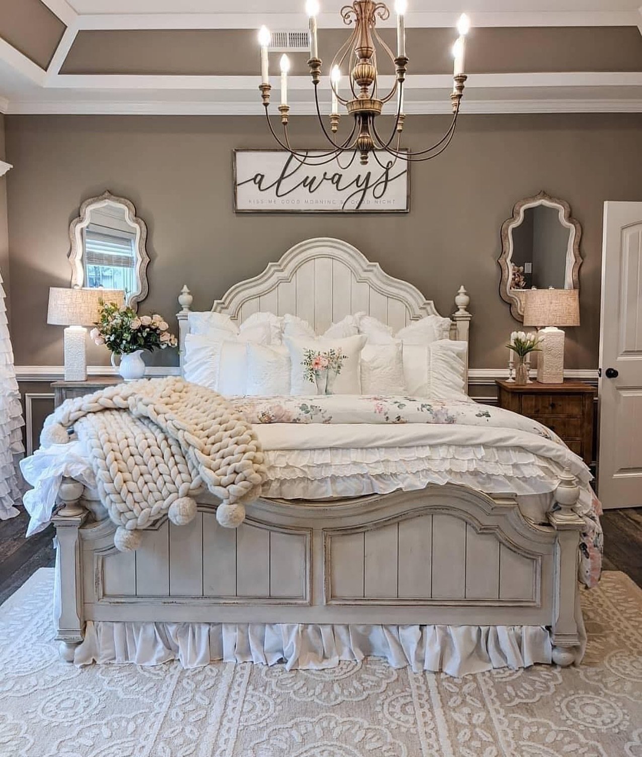 Feminine farmhouse bedroom with a large distressed white bed, ruffle bedding, and bronze chandelier.