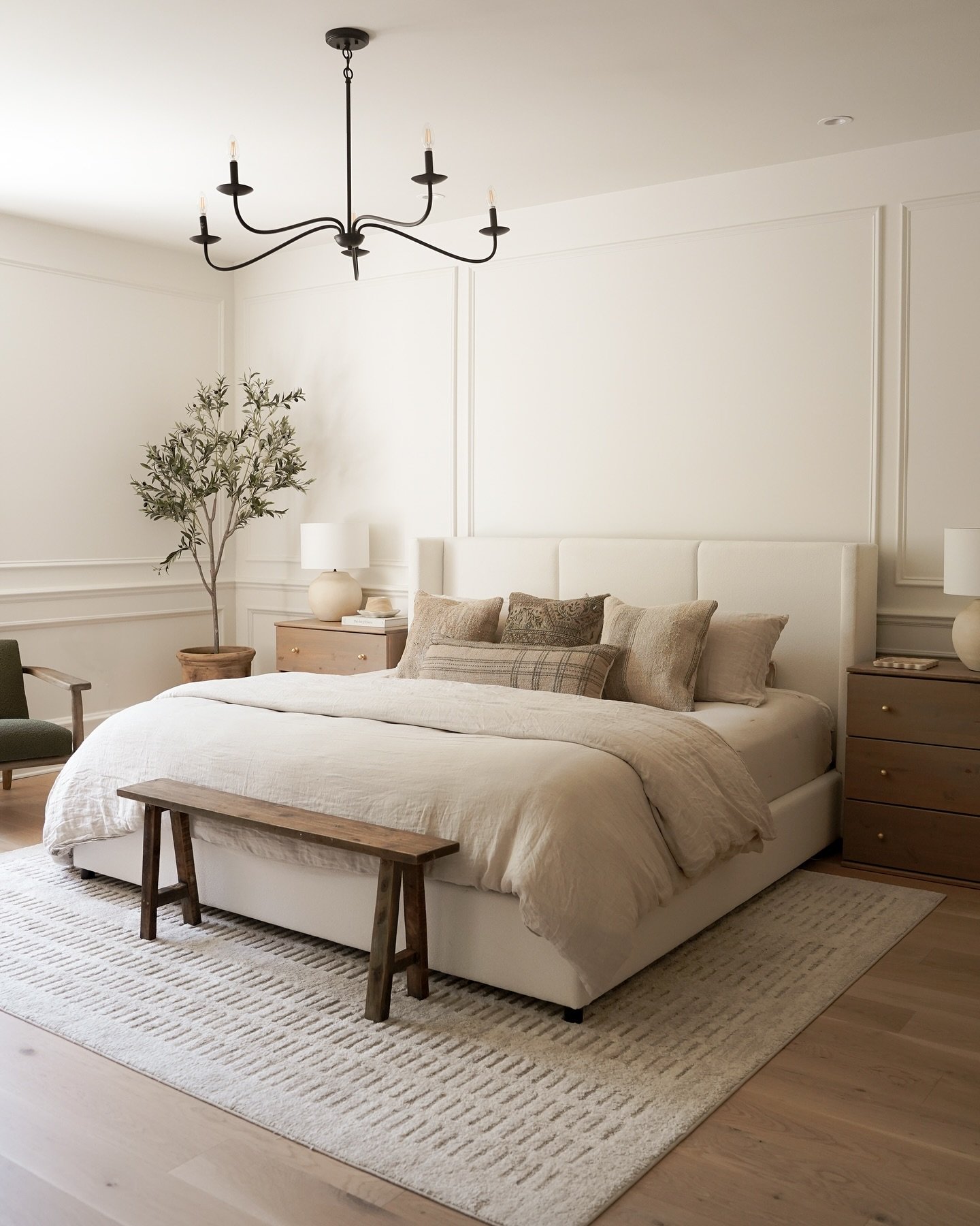 Master bedroom with warm neutral walls, floor-to-ceiling wall panel molding, a white upholstered bed with beige linens, and a black iron chandelier.