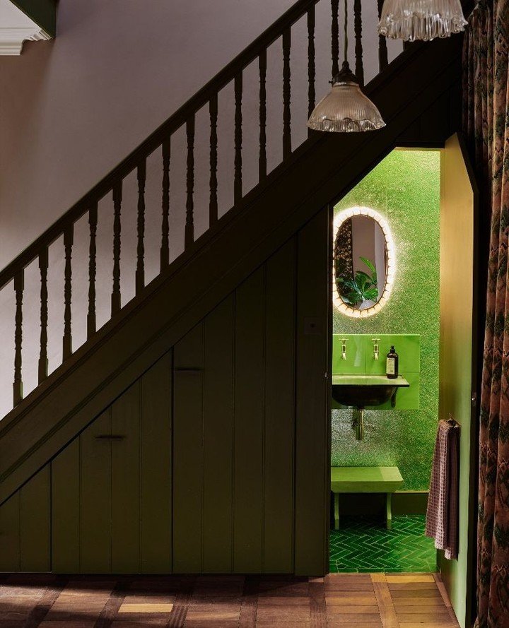 A brightly lit green powder room tucked beneath dark green staircase paneling.