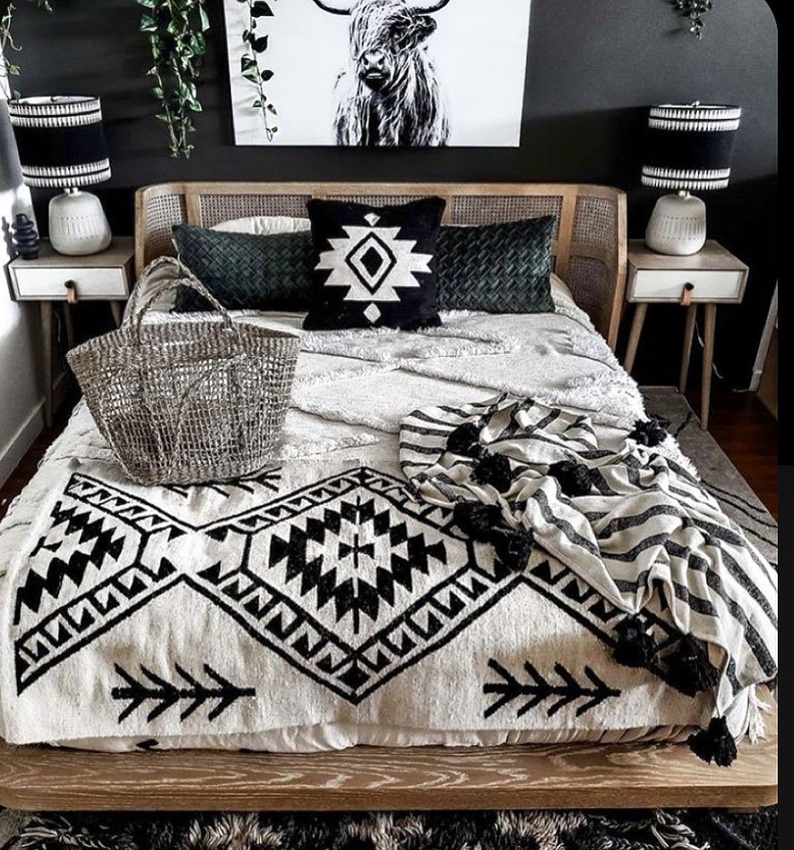 A contemporary Western bedroom with black walls, a light wood cane headboard, and layered bedding featuring bold black and white geometric patterns.