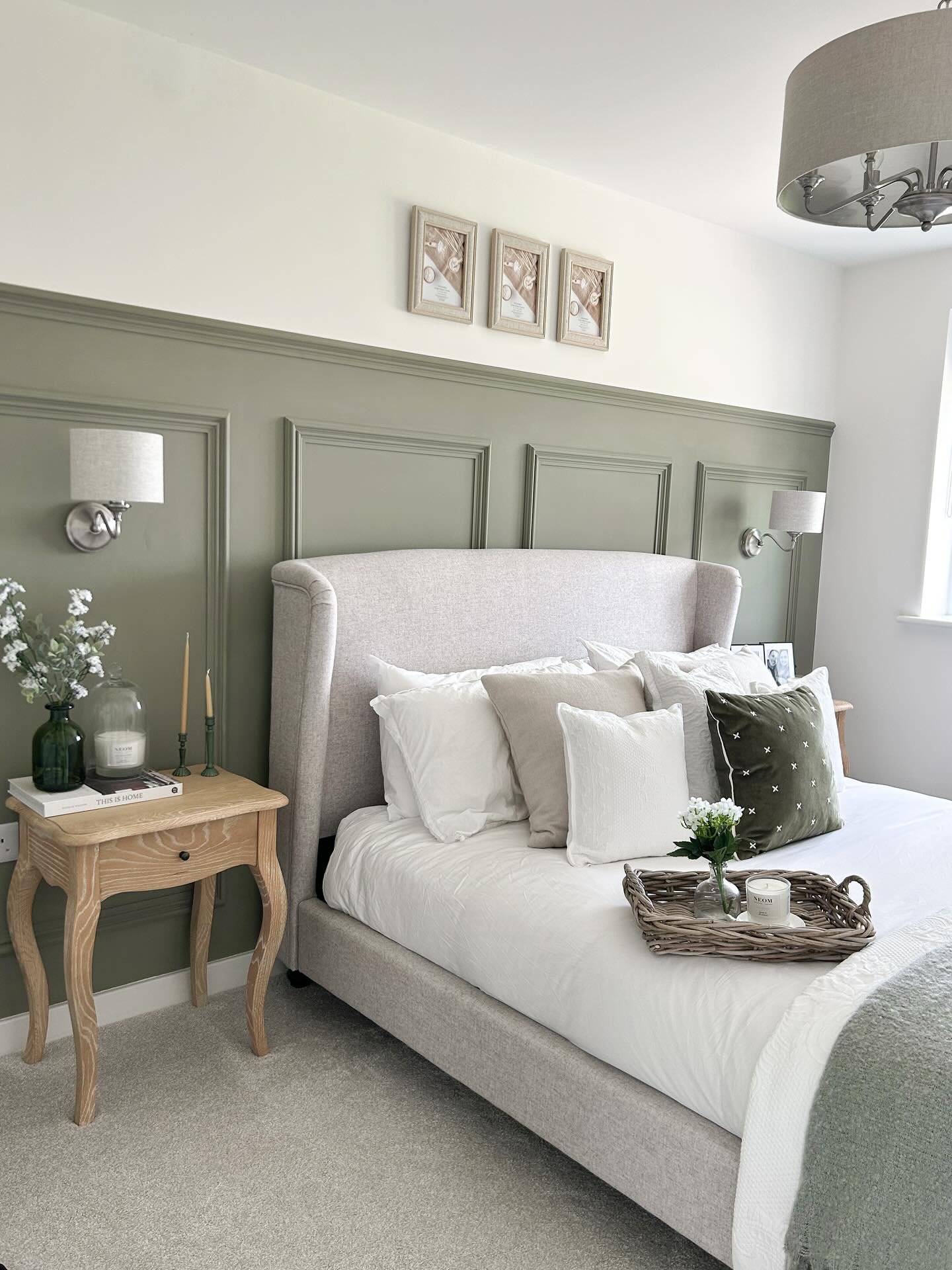 Bedroom with a rich sage green half-wall of decorative paneling behind a tall upholstered bed.