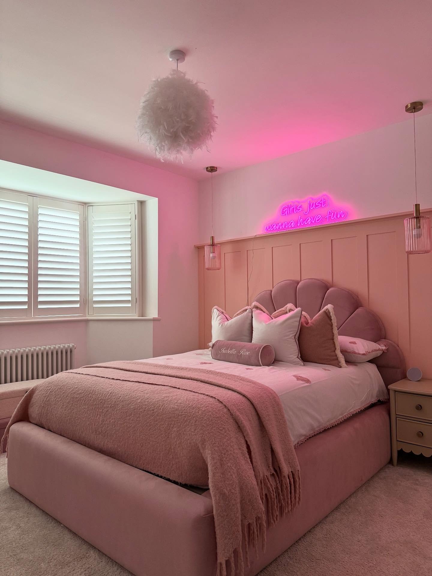 Modern girls bedroom with a scalloped velvet bed, a pink paneled feature wall, and a bright pink neon sign.