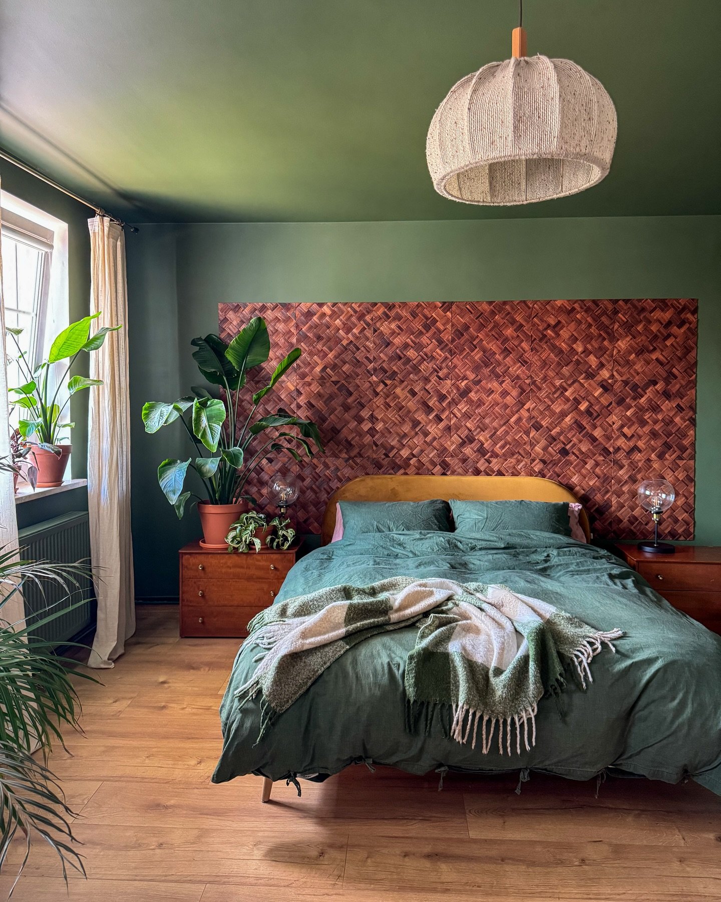 Green bedroom with a moss-green painted ceiling and walls, featuring a large woven wood headboard.