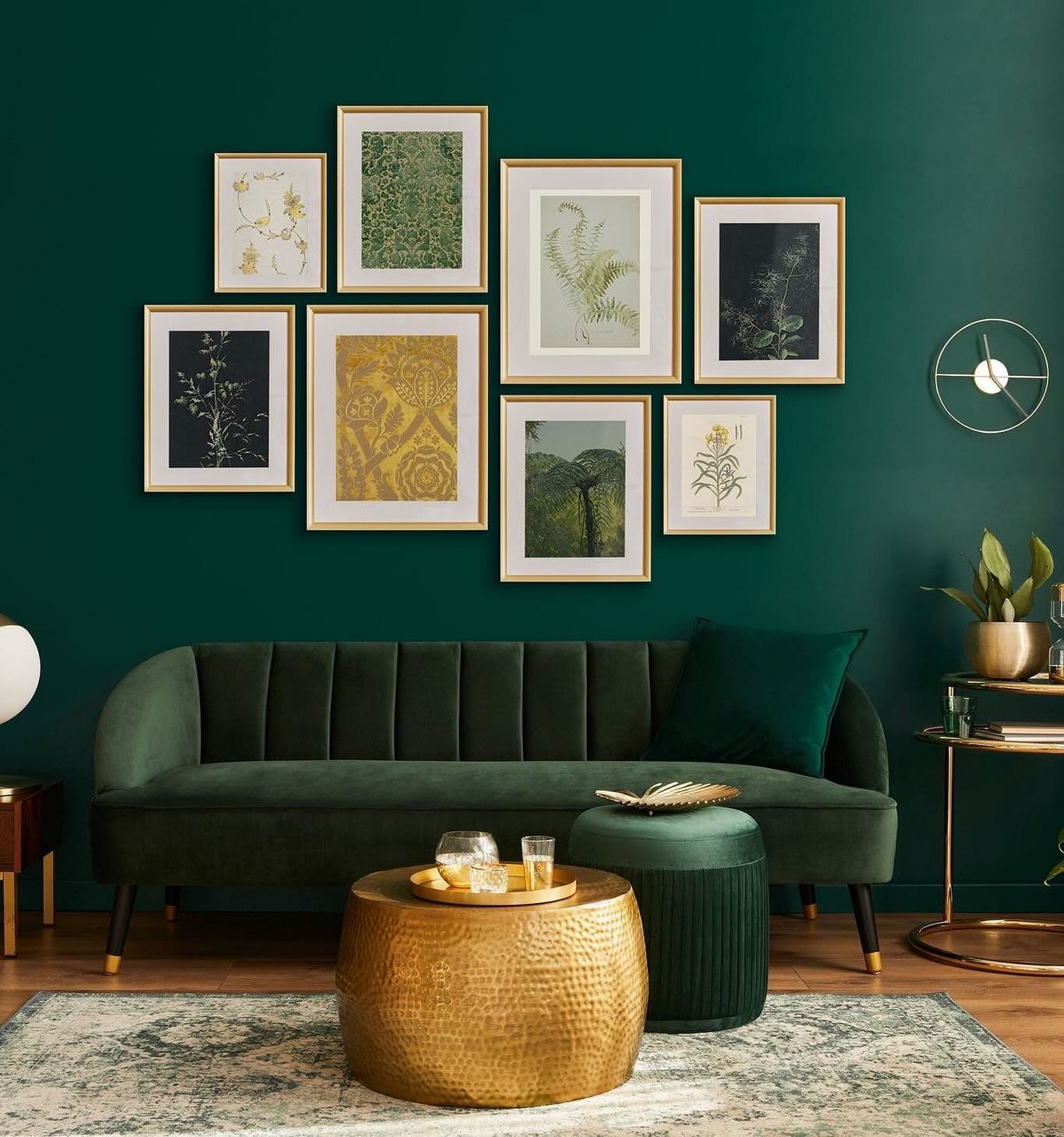 Asymmetrical cluster gallery wall of seven gold-framed botanical and damask prints against a dark emerald green wall above a green velvet sofa.