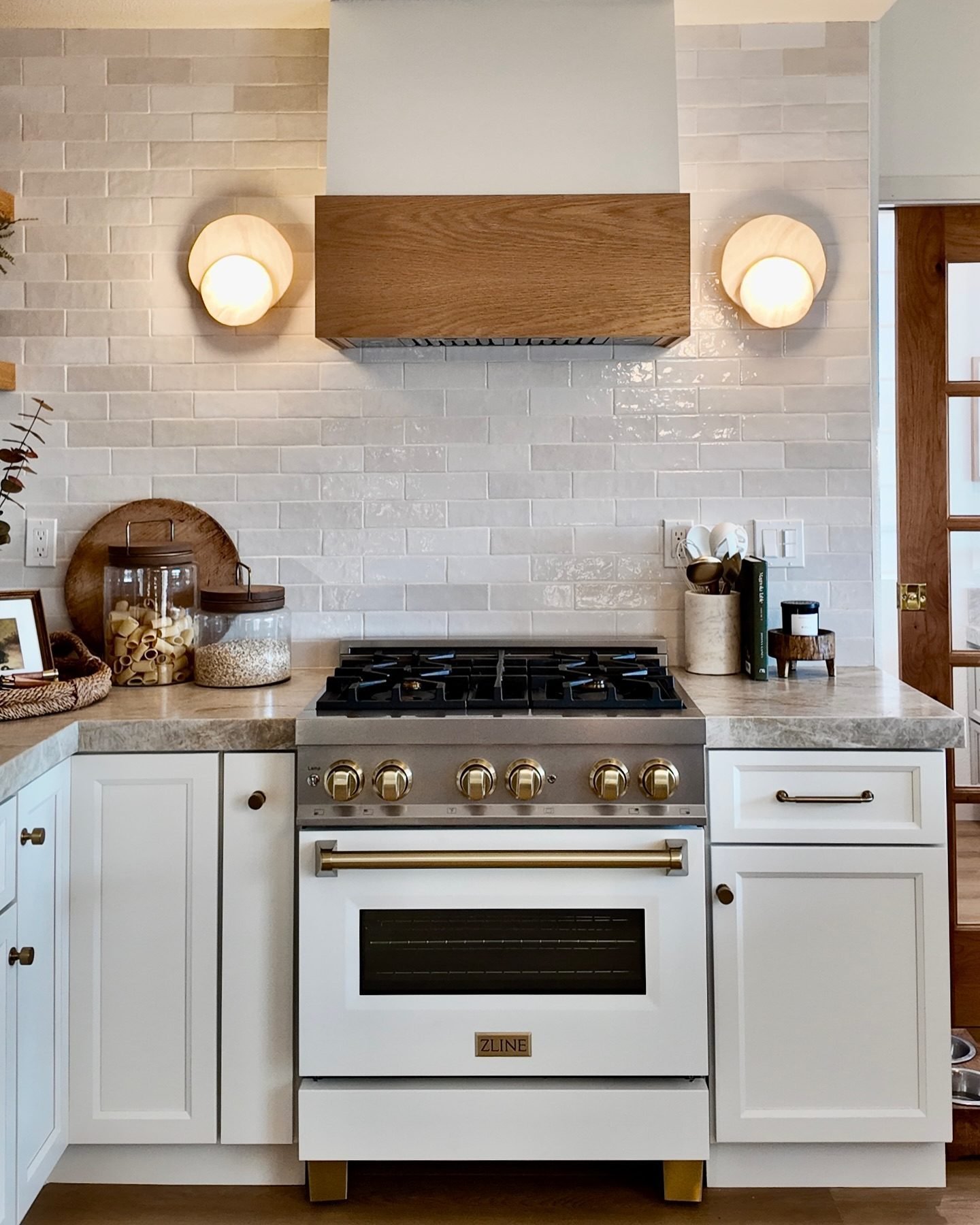 Transitional kitchen area with a glossy, irregular subway tile backsplash in light gray/white, a wood-front range hood, and a white and brass professional-style range.