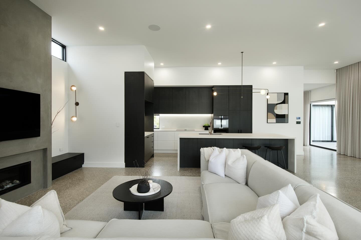 Modern open-concept living area with white sofa, black kitchen cabinetry, concrete fireplace, and terrazzo floor.