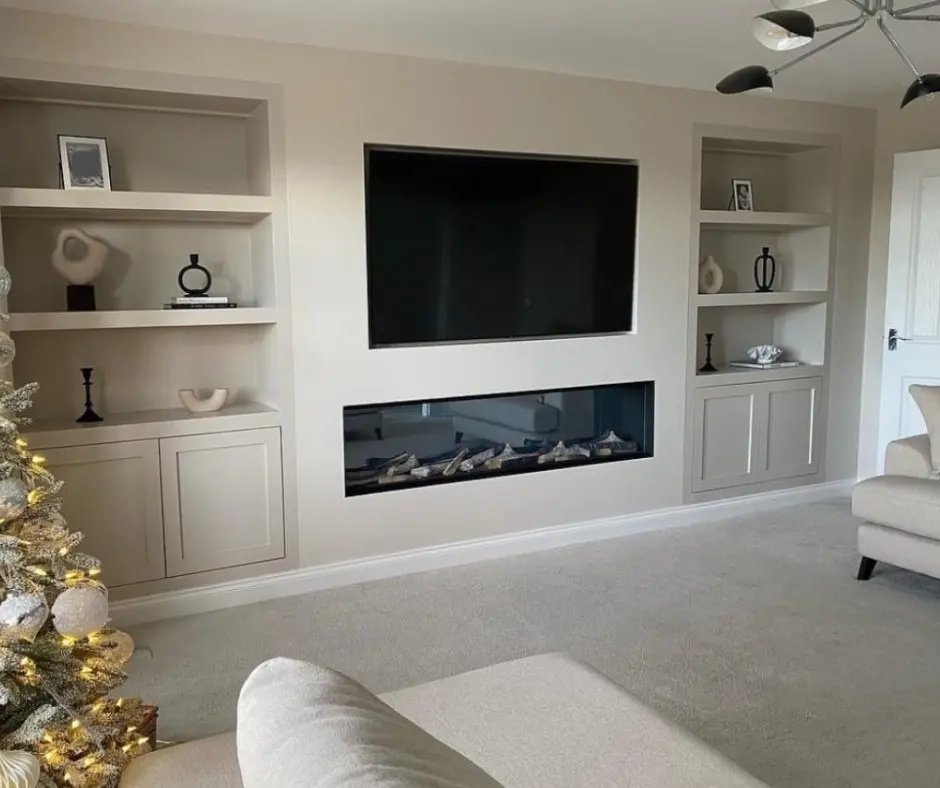 Minimalist living room with a linear, recessed electric fireplace and TV built into a greige-colored wall, flanked by matching alcove shelving units with bottom cabinets.
