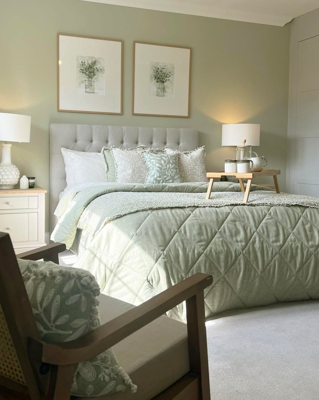 Bright bedroom with pale sage green walls and bedding, featuring a tufted grey headboard and white furniture.