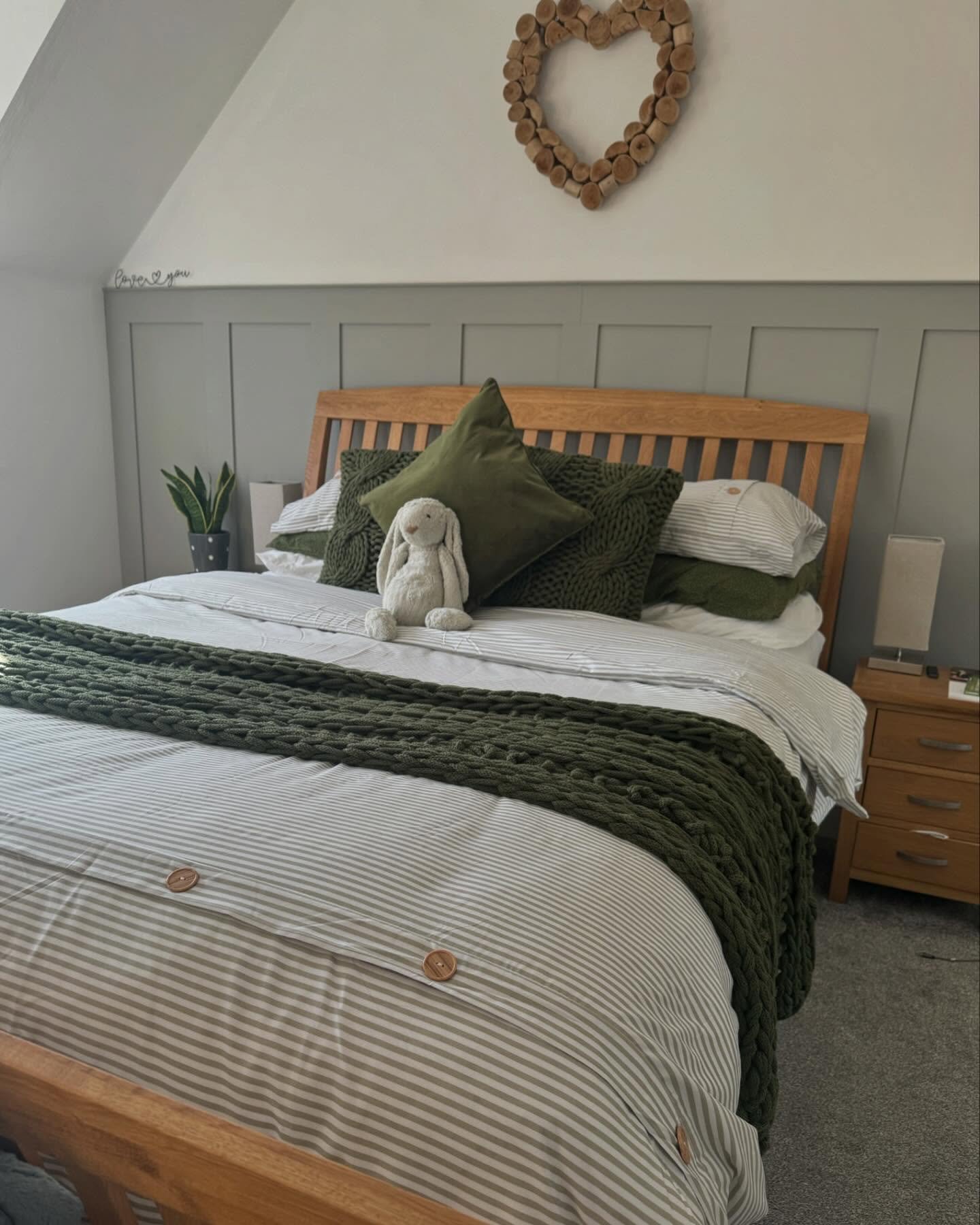 A cozy bedroom featuring a wooden bed, a gray vertical panel wall, striped bedding, and a chunky knit olive green throw blanket.