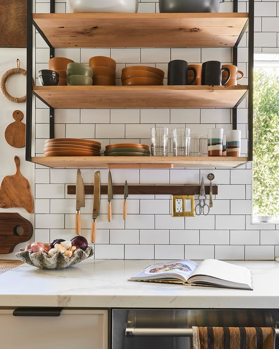 Kitchen featuring floating wood and black metal shelves over white subway tile backsplash, with dishes and a magnetic knife strip underneath.