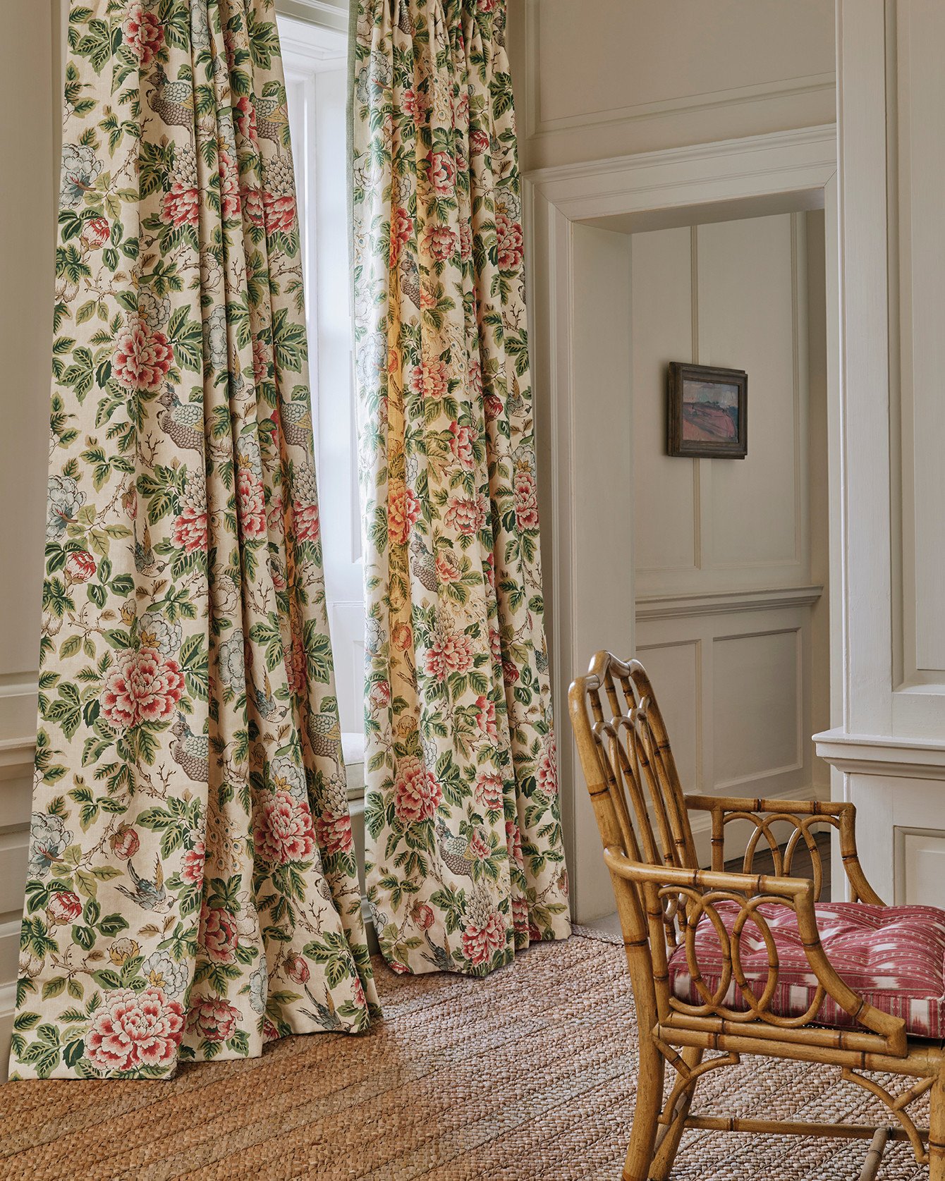 Floor-length curtains in a traditional floral chintz fabric with red and green tones, next to a bamboo chair and natural fiber rug.