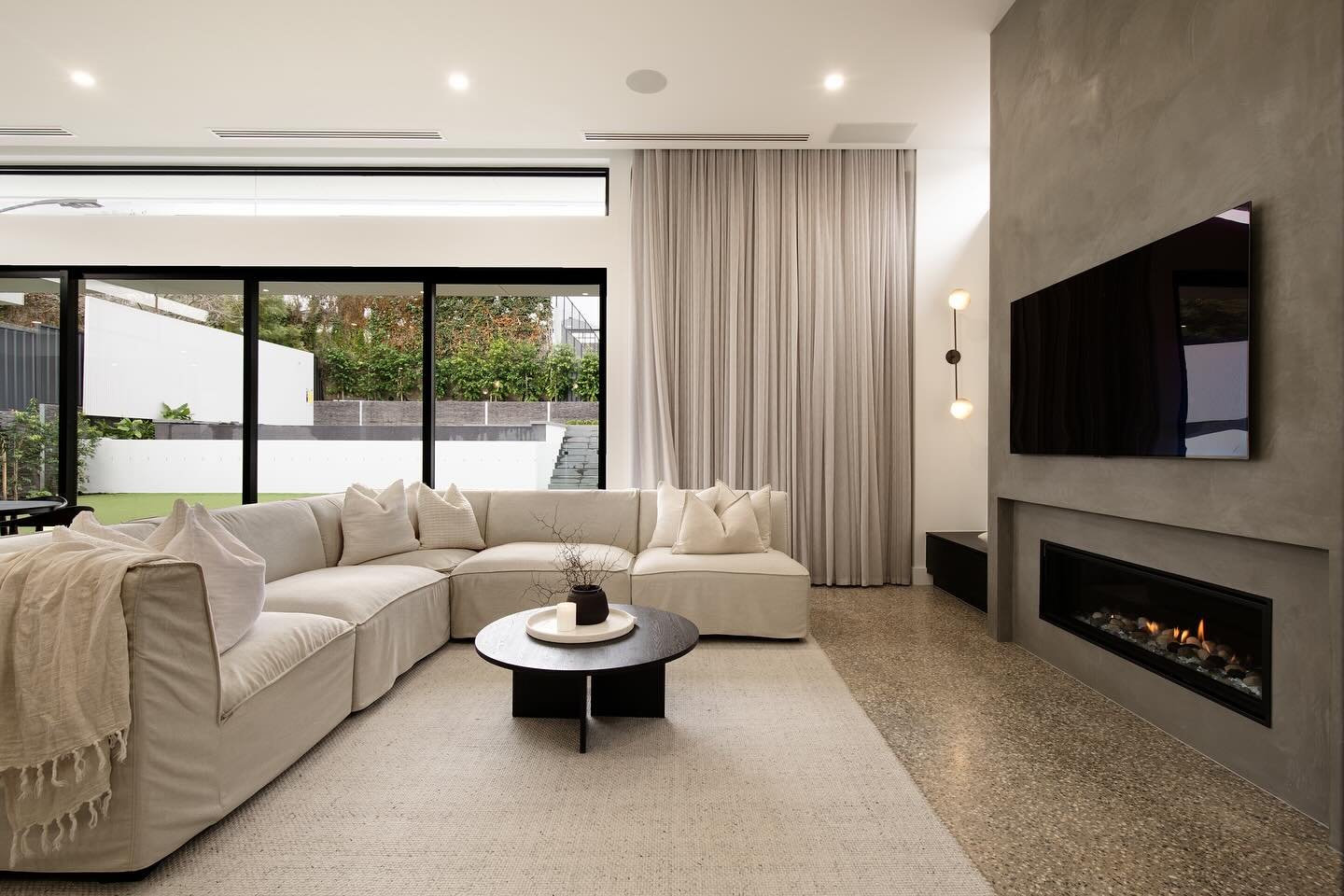 Cream sectional sofa on a light rug facing a gas fireplace set into a gray concrete-look wall.